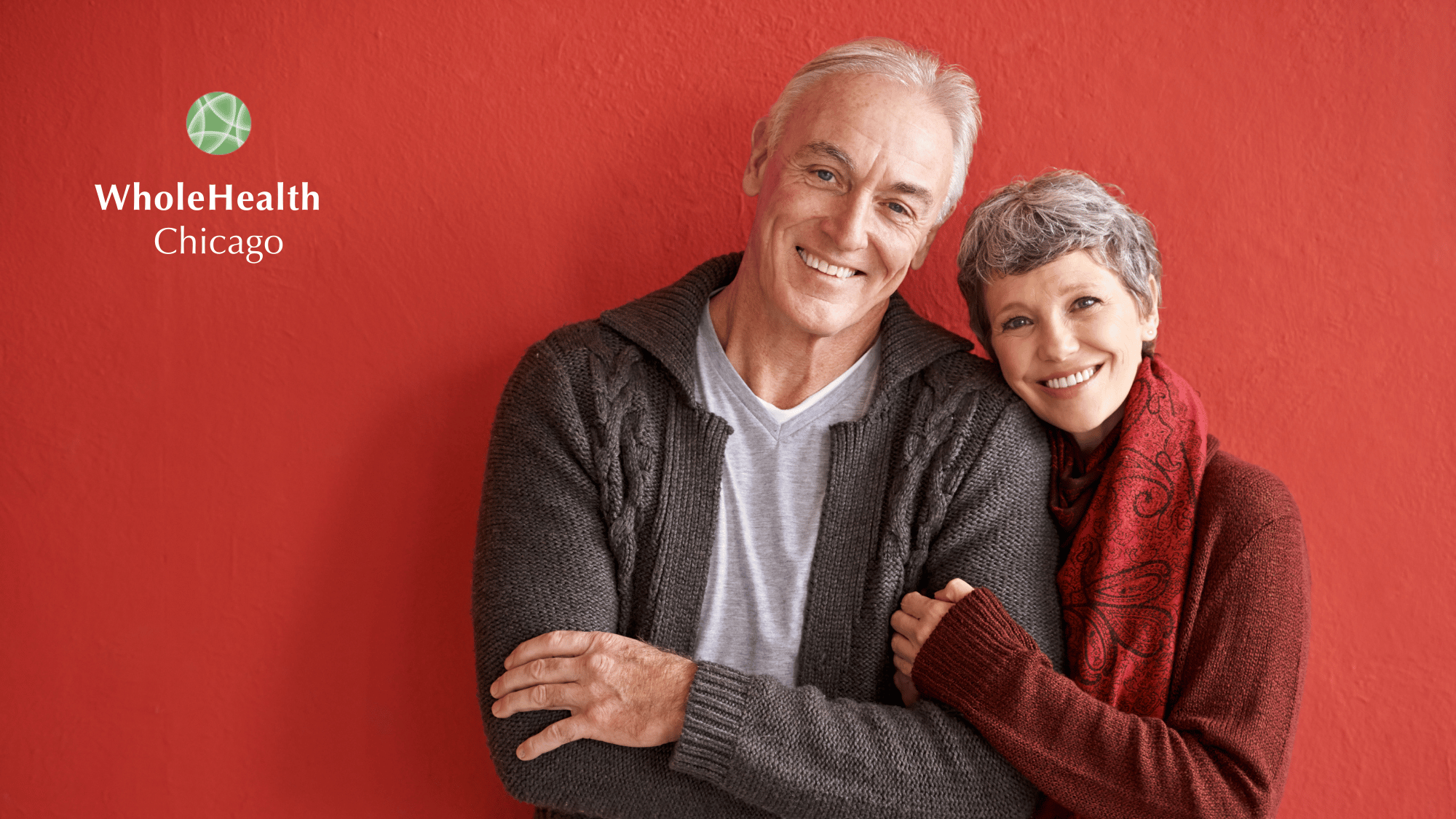 Smiling senior couple embracing in cozy sweaters, representing healthy aging and vitality—WholeHealth Chicago logo on a red background.